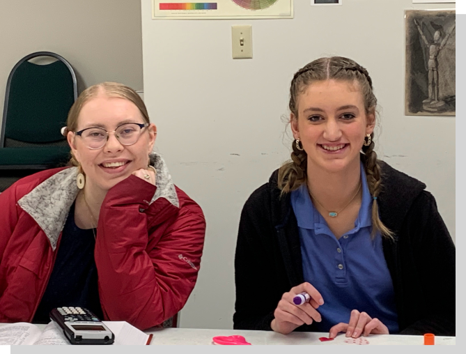 Two girls sitting at a table with pens and pencils.