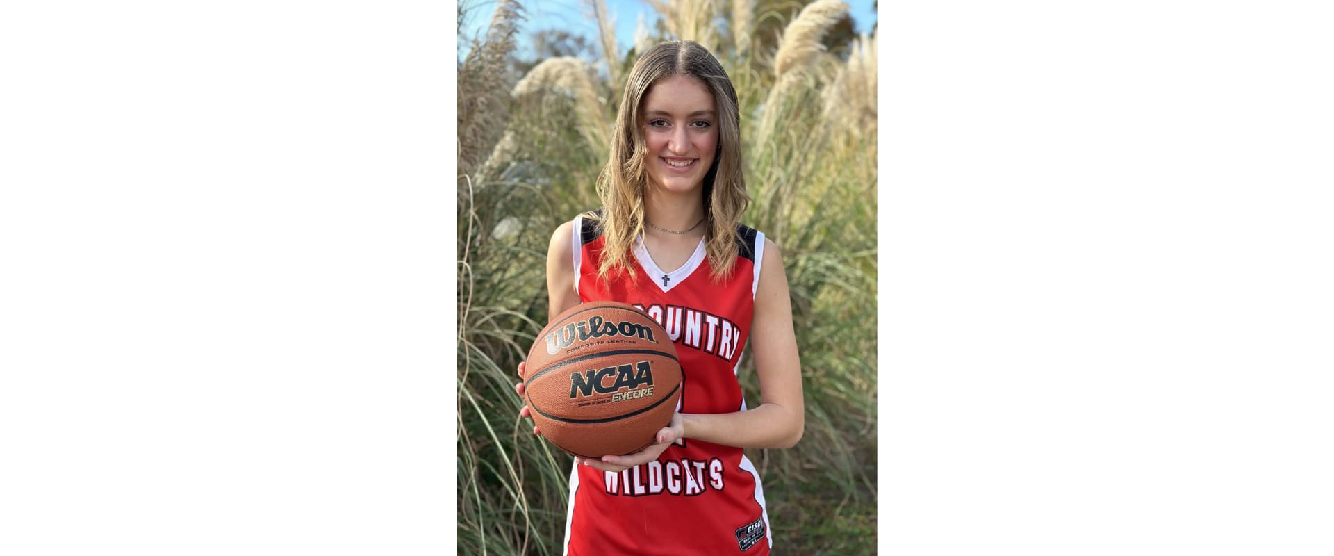 A girl holding a basketball in front of some tall grass.