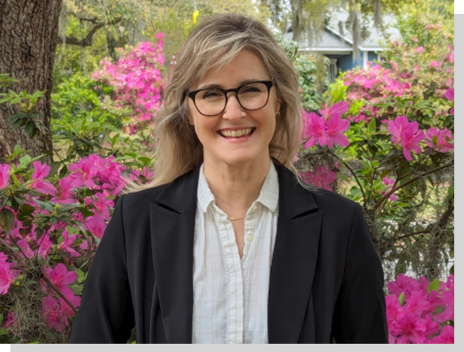 A woman with glasses standing in front of pink flowers.