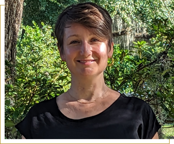 A woman standing in front of trees smiling for the camera.