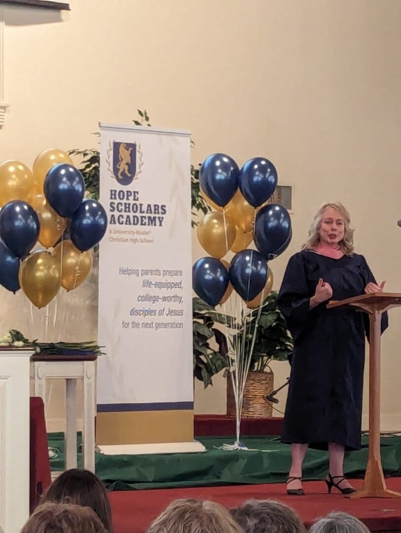 A woman standing at the podium in front of balloons.