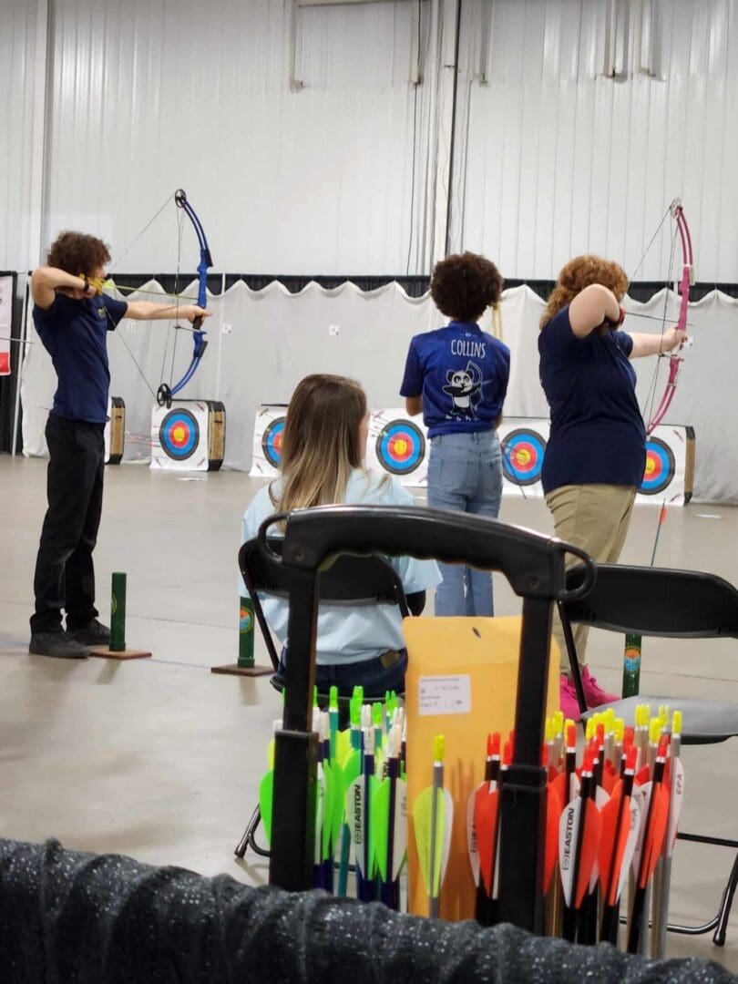 A group of people are practicing archery in an indoor arena.