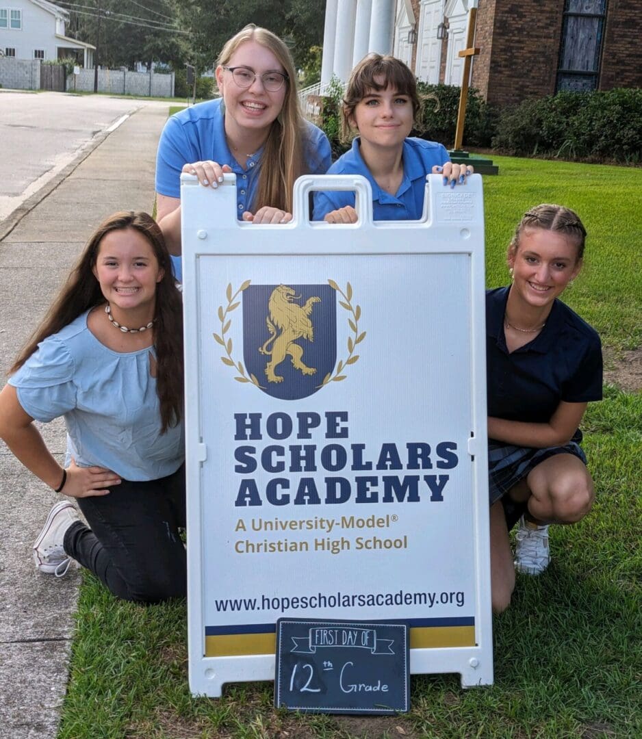 Four girls posing with a sign in front of them.