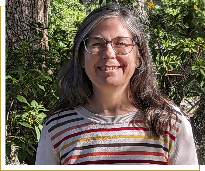 A woman with long hair and glasses is smiling.