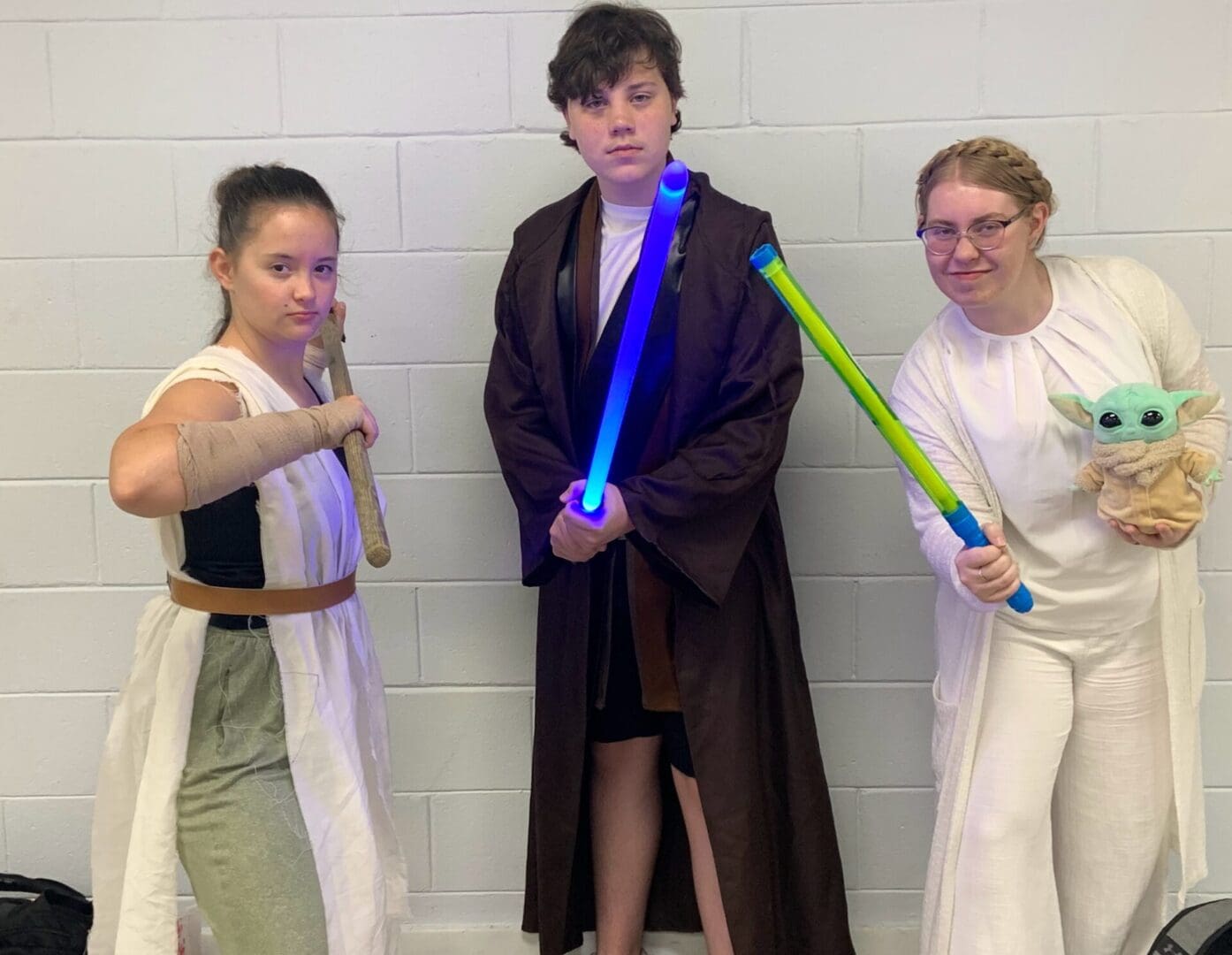 Three people are holding light sabers in a room.