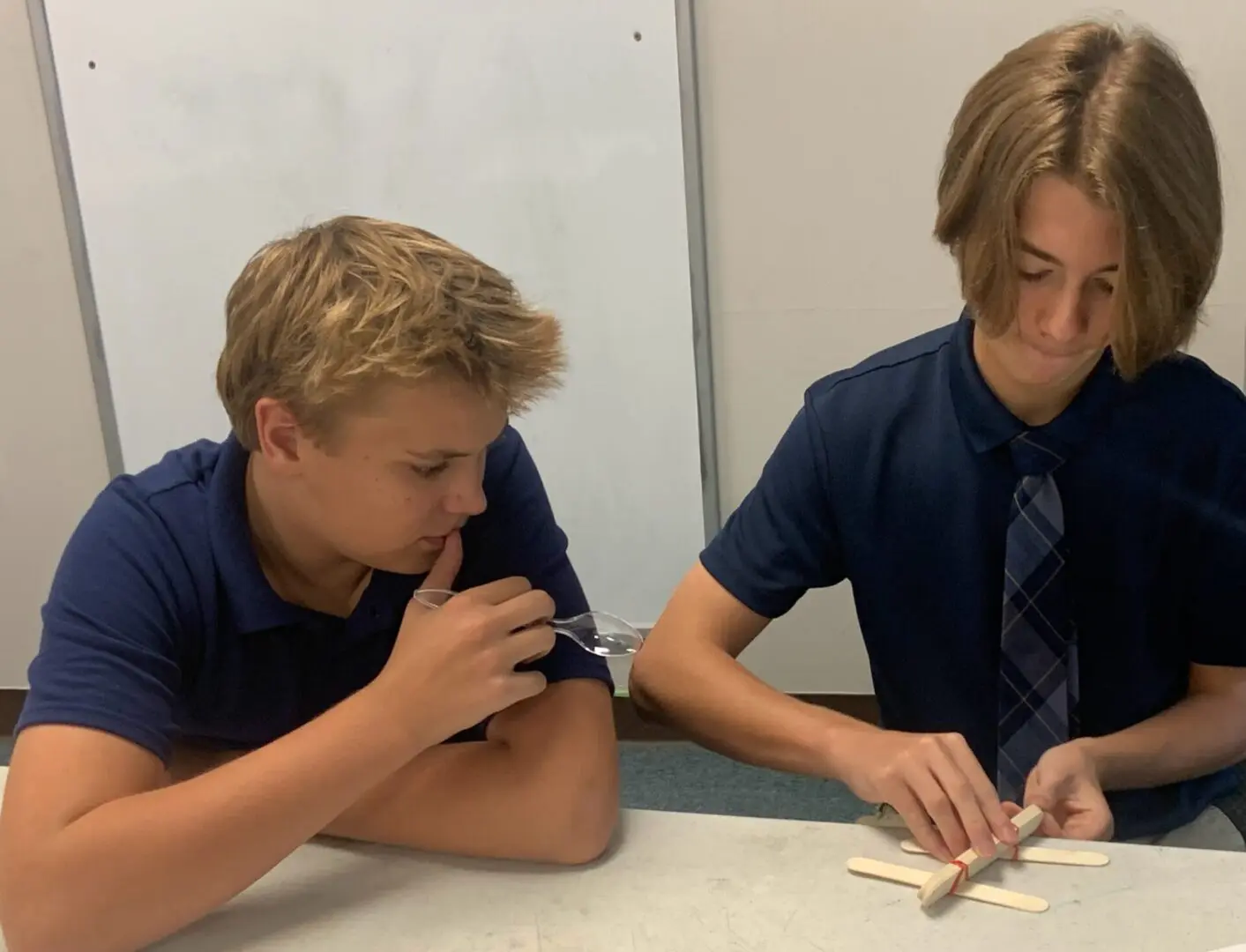 Two boys are sitting at a table and one of them is using a pair of scissors.