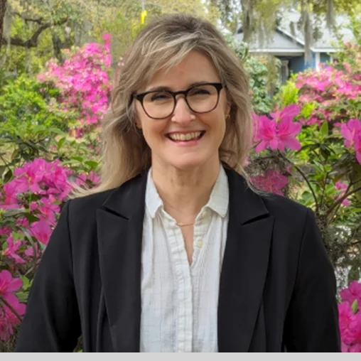 A woman with glasses standing in front of pink flowers.